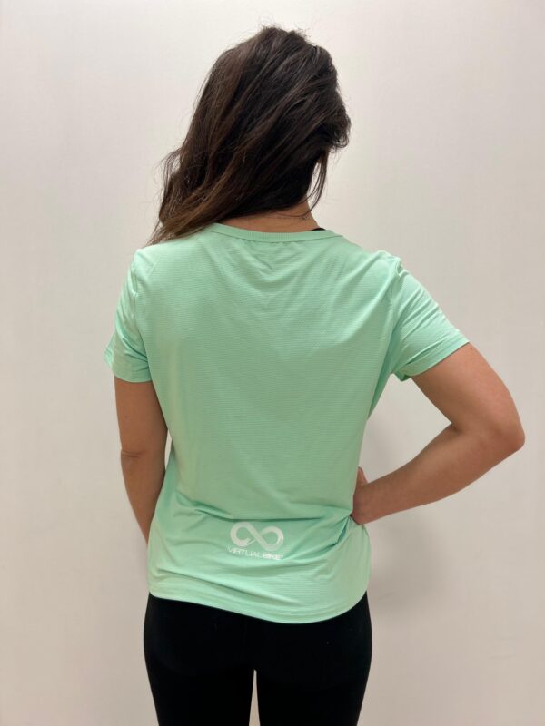 Mujer de espaldas utilizando una polera verde pastel con logo de Virtual Bike en la espalda